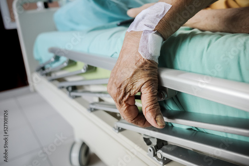 Wrinkled hand of a female elderly patient on bed handrail in a hospital ward