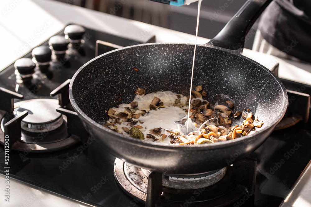 Close up of professional Chef cook hands roasts champignons mushrooms with cream in wok pan for Mediterranean cuisine. Close up of professional Chef cook hands roasts champignons mushrooms with cream in wok pan for Mediterranean cuisine.