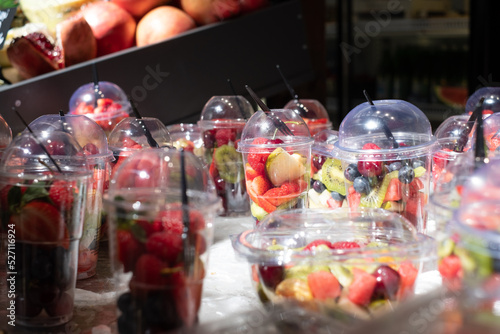Delicious, colourful, fresh berries and fruit pieces salad in plastic glasses placed on ice table. Blurred background. 