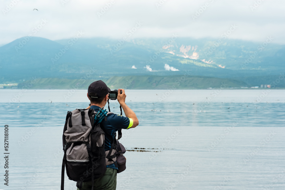 Obraz premium male tourist with a backpack photographs a foggy sea bay