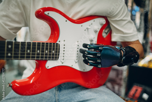 Young disabled man with artificial prosthetic hand plays on strings electric guitar at shop