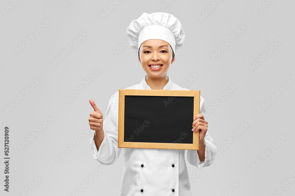 cooking, advertisement and people concept - happy smiling female chef holding black chalkboard showing thumbs up over grey background