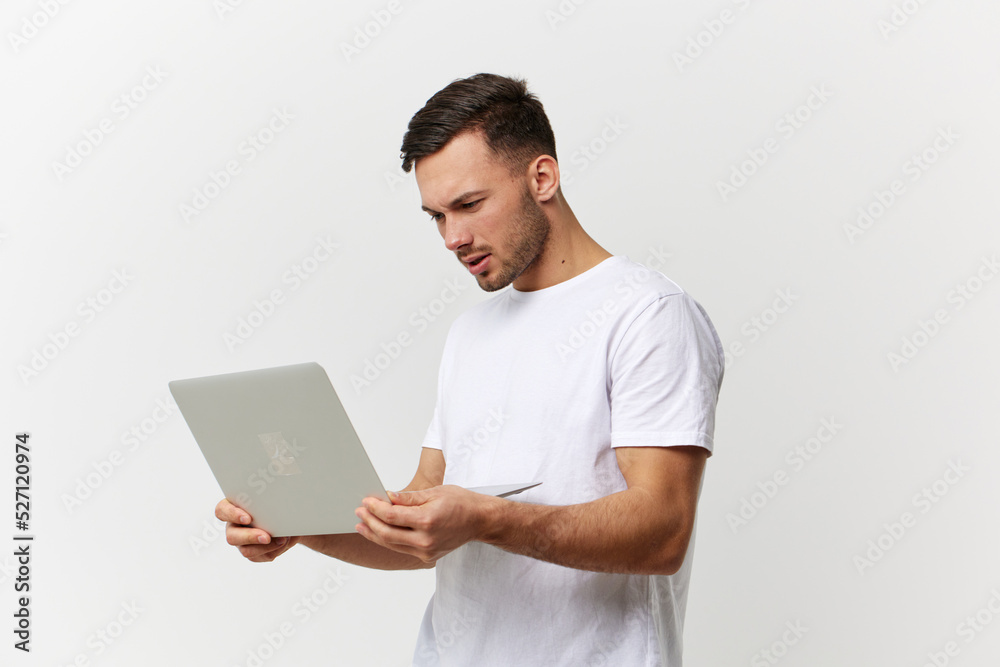 Unhappy angry tanned handsome man in basic t-shirt have problem with broken laptop posing isolated on over white studio background. Copy space Banner Mockup. Electronics repair IT concept Unhappy angry tanned handsome man in basic t-shirt have problem with broken laptop posing isolated on over white studio background. Copy space Banner Mockup. Electronics repair IT concept