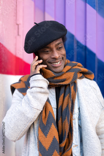 Portrait of smiling young adult African American man talking on phone. He is isolated on a multicolored wall.