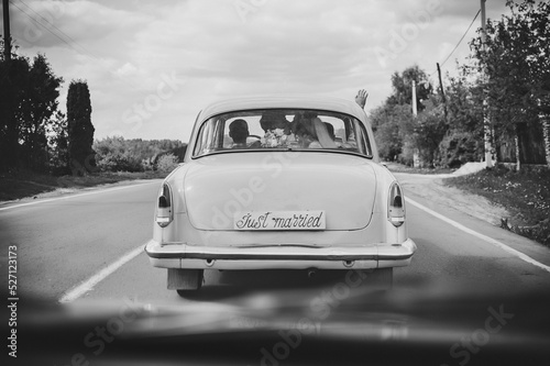 Happy bride kiss groom, newlywed wedding couple is driving a retro car on a country road for honeymoon after the ceremony. Way. The best day and marriage. Just married. Black and white photo.