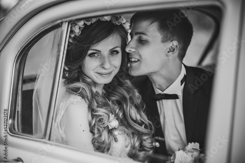 Happy bride and groom, newlywed wedding couple is sitting in a retro car on a country road for honeymoon after the ceremony. The best day and marriage. Just married. Black and white photo.