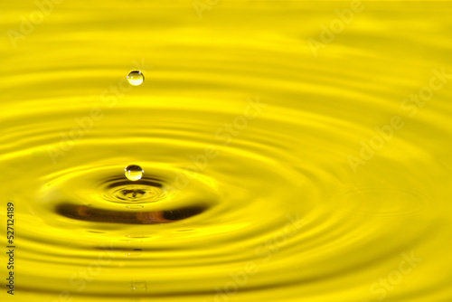 Splash drop of water with diverging water circles, on yellow background.