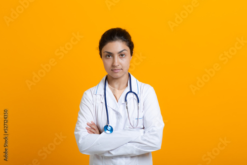 Portrait of indian doctor woman in white medical gown stethoscope isolated on yellow background.