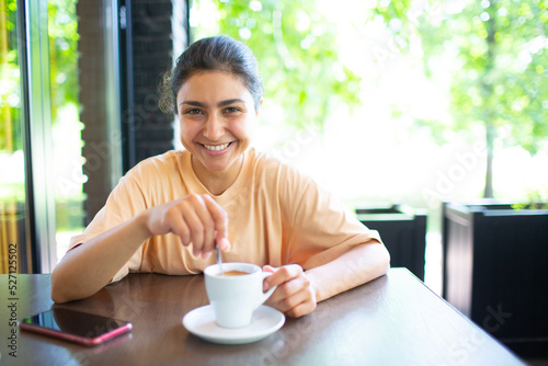 Smiling lovely young indian woman drinking coffee at outside cafe