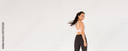 Full length of active and healthy good-looking asian fitness girl, sportswoman turn behind at looking at camera with satisfied face, gym coach encourage start training, white background