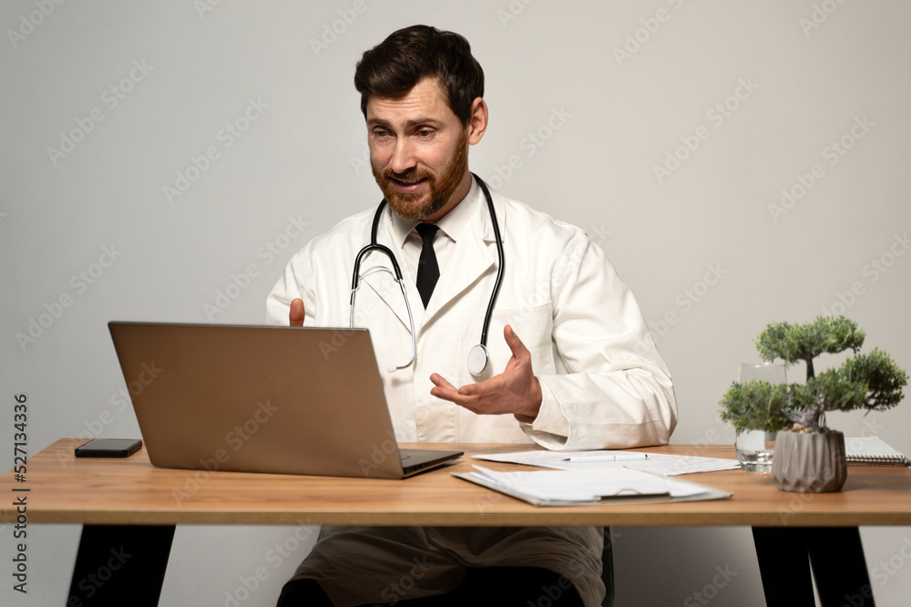 Waist up portrait view of the happy doctor having video call using laptop while sitting