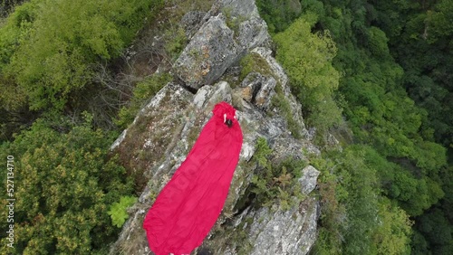 A girl in a red dress sits on the edge of a cliff, summer, mountains and forest, a seed from a drone