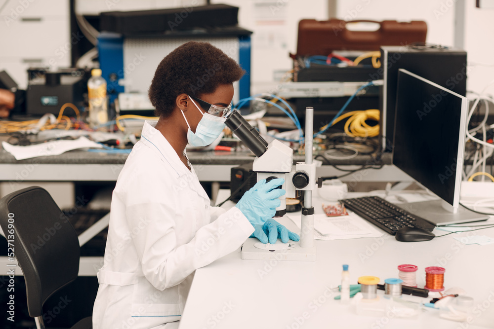 Scientist african american woman in face mask and gloves working in laboratory with electronic tech instruments and microscope. Research and development of electronic devices by color black woman. Scientist african american woman in face mask and gloves working in laboratory with electronic tech instruments and microscope. Research and development of electronic devices by color black woman.