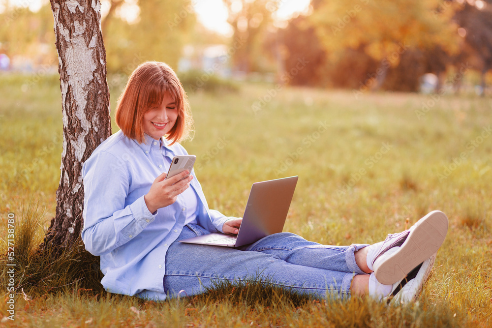 Photo portrait of a beautiful young woman smiling with her teeth, sitting in a green park and working on a laptop and looking at the phone smiling Photo portrait of a beautiful young woman smiling with her teeth, sitting in a green park and working on a laptop and looking at the phone smiling