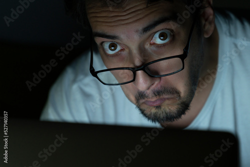 Close up of disgusted face of shocked man looking at laptop at the night time