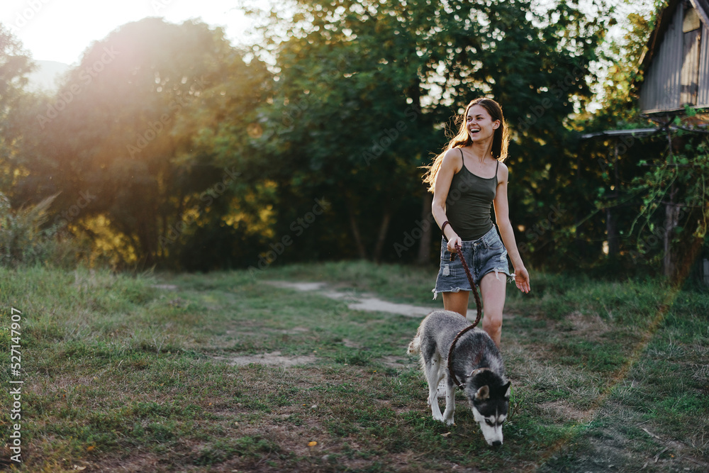 A woman runs and jumps playing with her dog in the summer in a park among greenery in nature outside the house. Lifestyle in sports and walking with a husky dog on a leash A woman runs and jumps playing with her dog in the summer in a park among greenery in nature outside the house. Lifestyle in sports and walking with a husky dog on a leash