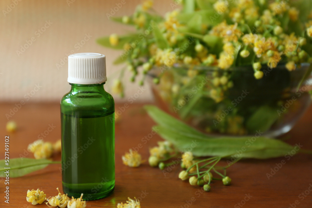 Bottle of essential oil and linden blossoms on wooden table, closeup. Space for text Bottle of essential oil and linden blossoms on wooden table, closeup. Space for text