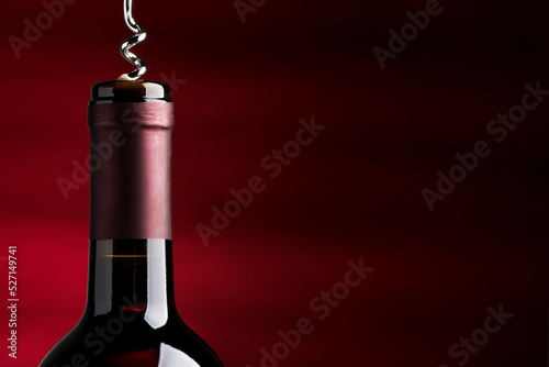 Opening bottle of wine with corkscrew on burgundy background. Space for text