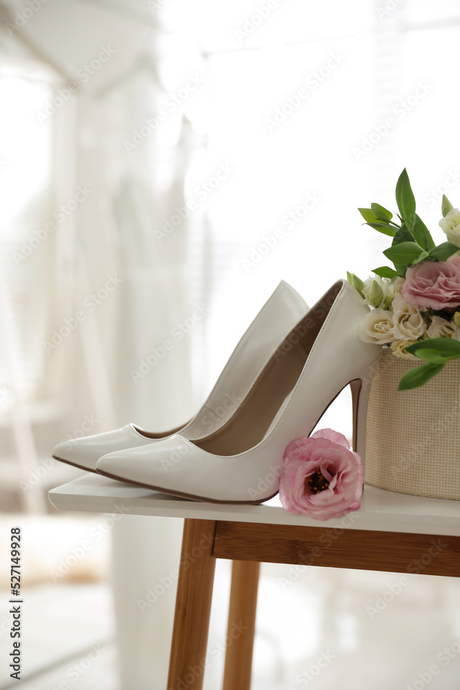 Pair of white high heel shoes, flowers and blurred wedding dress on background, space for text