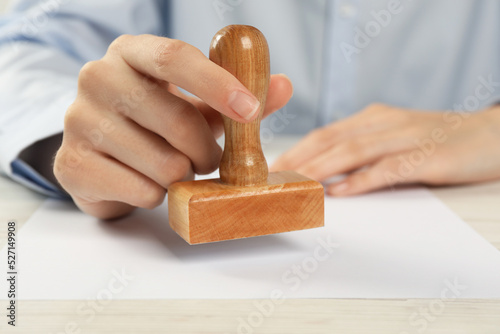 Woman stamping blank sheet of paper at white wooden table, closeup