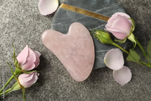 Rose quartz gua sha tool and flowers on grey table, flat lay photo