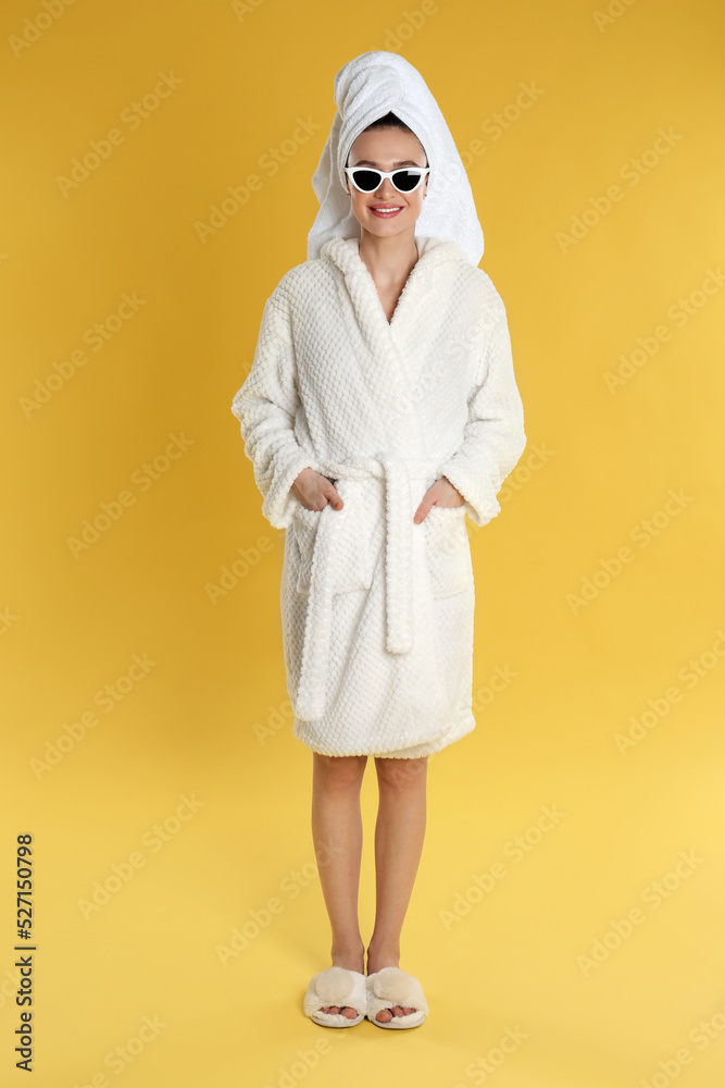 Beautiful young woman in bathrobe and sunglasses on yellow background