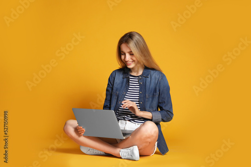 Young woman with laptop on yellow background
