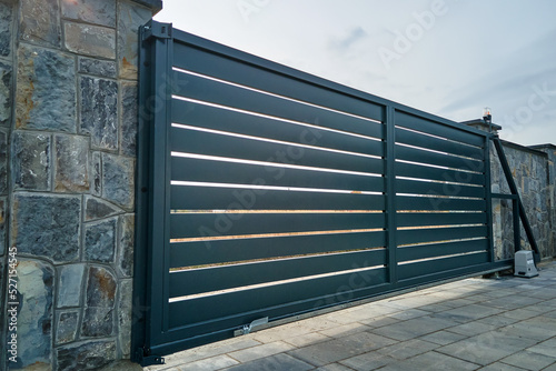 Foto Wide automatic sliding gate with remote control installed in high stone fense wall