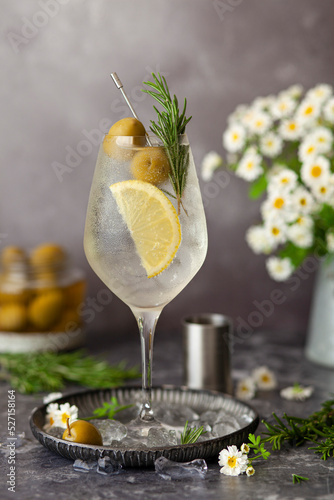 An Italian white spritz cocktail made with bianco bitter liqueur and garnished with lemon, olives and rosemary. photo