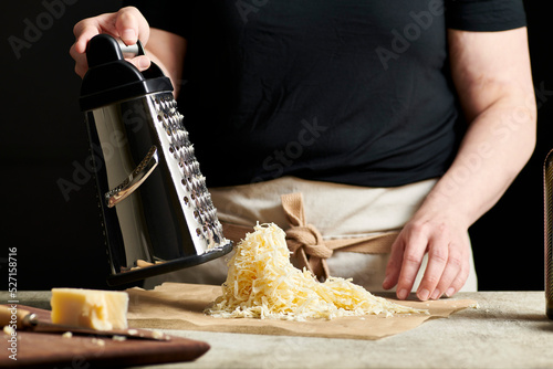 Hands grating cheese onto parchment paper.
