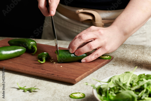 Hands slicing jalapenos on a cutting board. photo