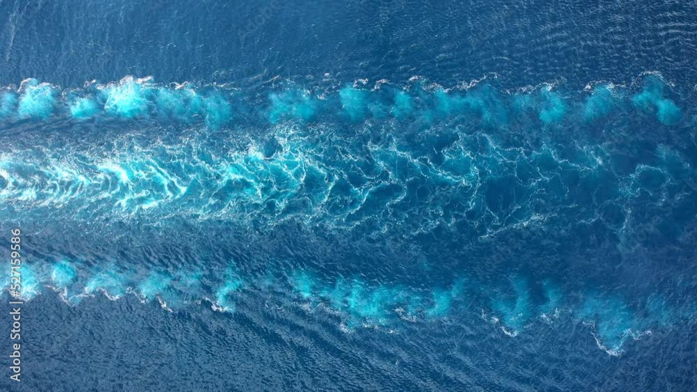Wake of a cargo ship texture on the sea surface. Engine roars at full speed and leaves wake water on the Ocean. Aerial top down view of water foam trace behind the tanker
