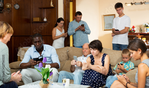 Large multiracial family sitting with mobile gadgets in cozy living room. Concept of family phubbing photo