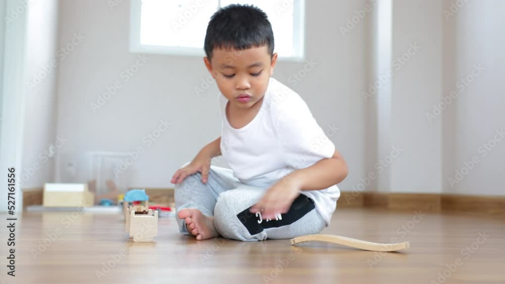 Attention asian boy playing wood block building rail way and road on the floor at home. Attention asian boy playing wood block building rail way and road on the floor at home.