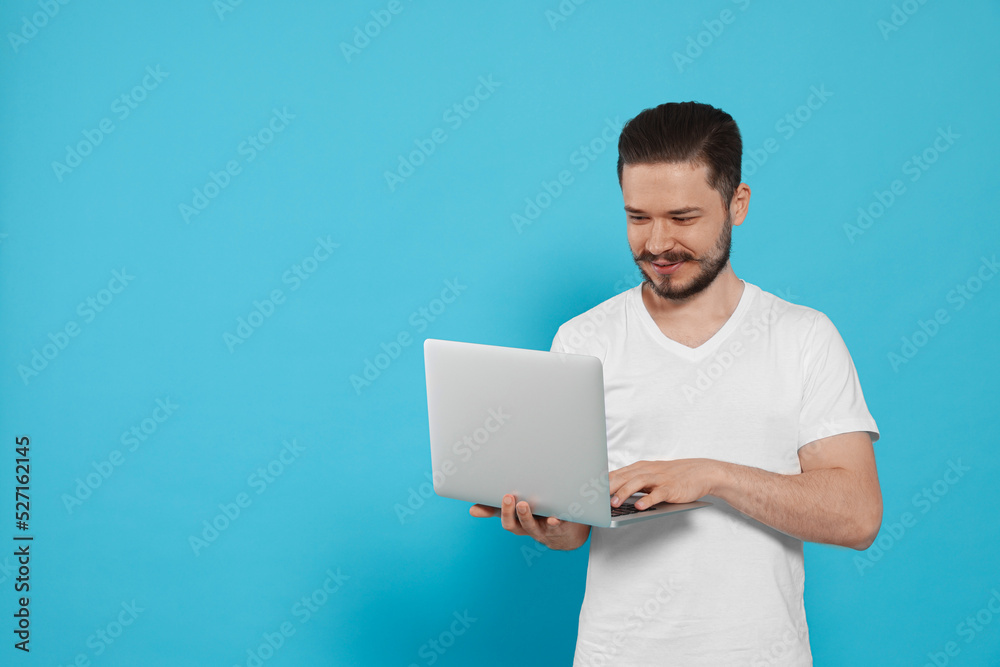 Smiling man using laptop on light blue background. Space for text Smiling man using laptop on light blue background. Space for text