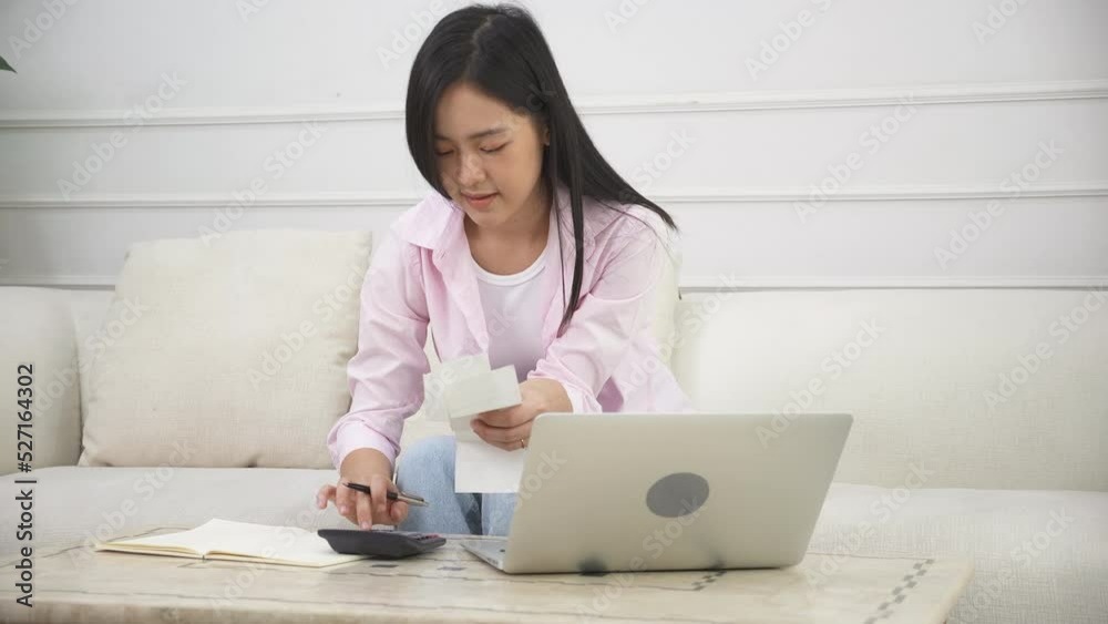 Young asian woman calculating finance household with calculator on desk at home, girl checking bill for saving and planning expenses, debt and loan, tax and accounting, business and financial concept. Young asian woman calculating finance household with calculator on desk at home, girl checking bill for saving and planning expenses, debt and loan, tax and accounting, business and financial concept.