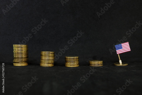 US economic recession, financial crisis and dollar depreciation concept. Flag of America in decreasing stack of coins in dark black background.