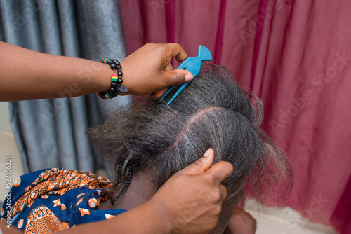 Hands of an hairdresser, stylist or entrepreneur making and weaving the grey hair of an elderly African Nigerian woman