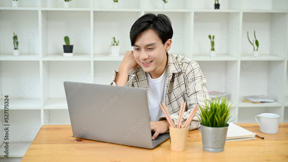 Smart and handsome young Asian male freelancer using his portable laptop computer. Smart and handsome young Asian male freelancer using his portable laptop computer.