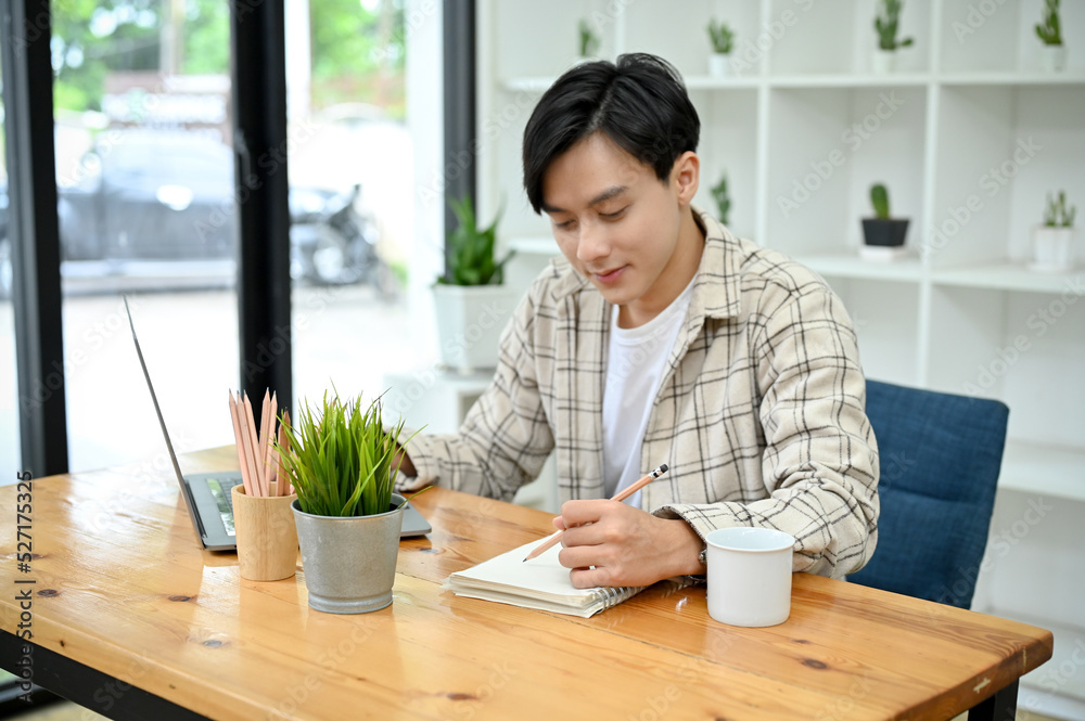 Handsome Asian male college student in coffee shop doing his homework, writing on his notebook Handsome Asian male college student in coffee shop doing his homework, writing on his notebook