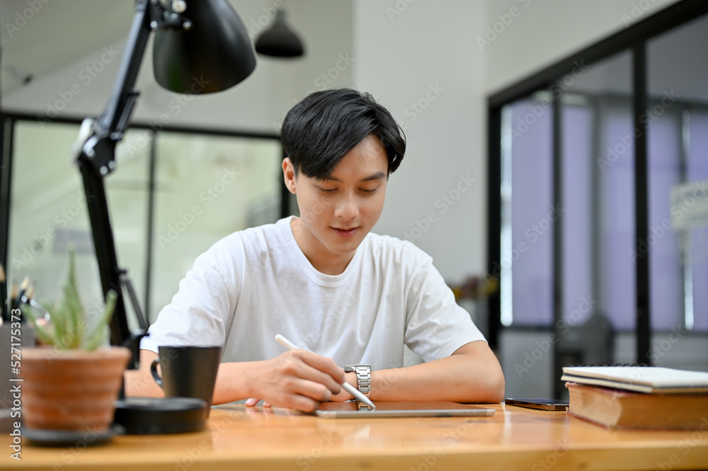 Good looking young Asian man at his working desk, using digital tablet Good looking young Asian man at his working desk, using digital tablet