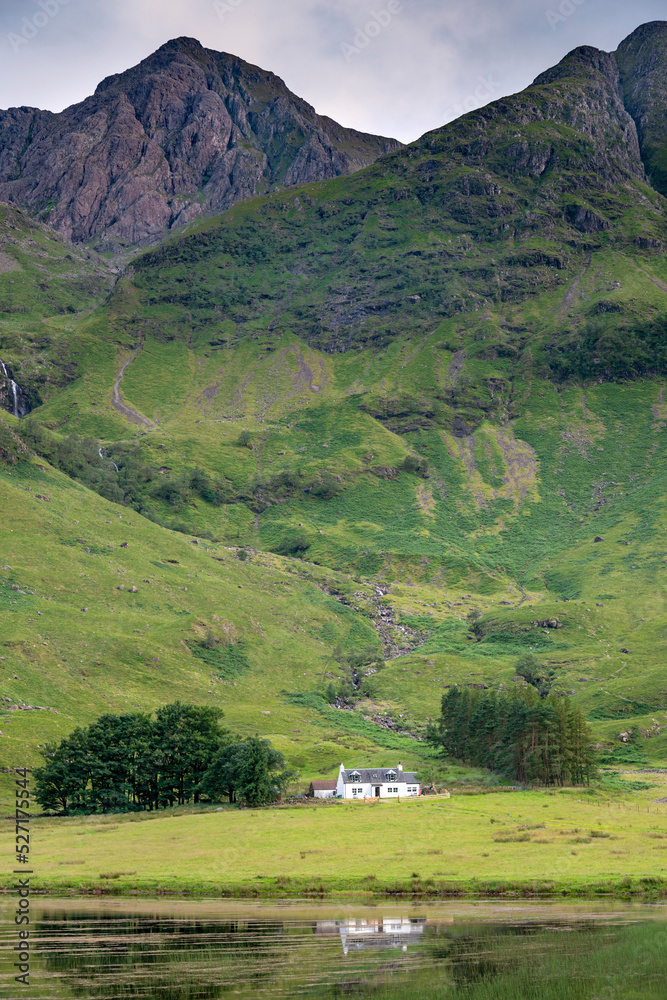 Small white cottage below magnificent mountains next to Loch Achtriochtan ,Glencoe,Scotland,UK.