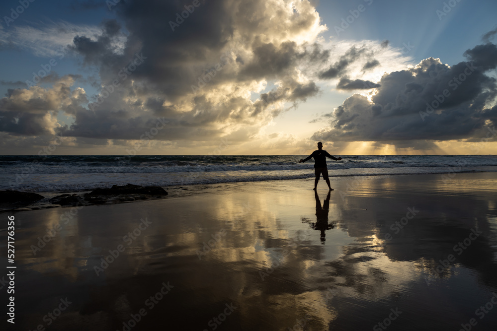 Silhouette of a man on the beach during sunrise. reflections in the water on the beach.