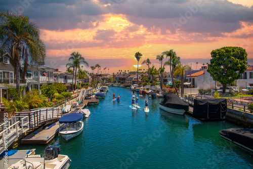 a gorgeous summer landscape at the Naples Canals with boats docked along the banks and people on paddle boards in the water, lush green palm trees and powerful clouds at sunset in Long Beach photo
