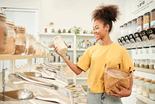 Young African American woman is choosing and shopping for organic products in refill store with reusable bag, zero-waste grocery, and plastic-free, eco environment-friendly, sustainable lifestyles.