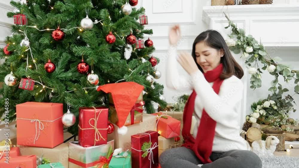 Woman wrapping christmas gift box under xmas tree. Asian woman decor bauble ball christmas tree in xmas holiday winter seasonal celebration. Close up woman hands wrap present gift in cozy living room Woman wrapping christmas gift box under xmas tree. Asian woman decor bauble ball christmas tree in xmas holiday winter seasonal celebration. Close up woman hands wrap present gift in cozy living room