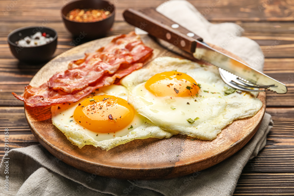 Plate of tasty fried eggs with bacon on wooden table, closeup