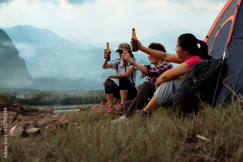 Asian young people groups sit enjoy with beer and drinking near a camping tent with mountain views of natural rainforest in foggy weather. Enjoying nature in background.