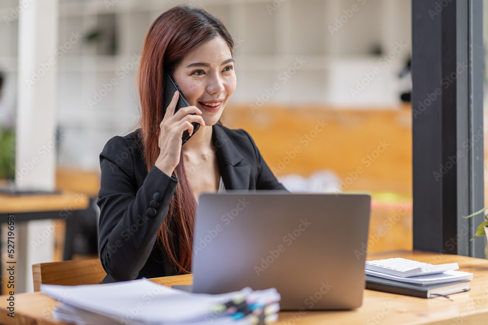 Young Business Asian woman talking on a smartphone and sitting on desk in workplace, Asian female Business accountant Documents data sitting at his workplace. Young Business Asian woman talking on a smartphone and sitting on desk in workplace, Asian female Business accountant Documents data sitting at his workplace.