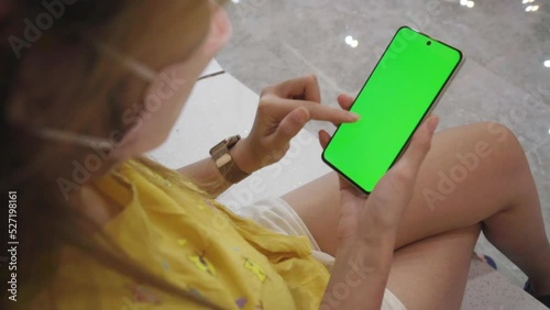 Women's hand showing vertical smartphone with mock-up chroma key greenscreen on outdoor background. Young person with modern phone Greenscreen
